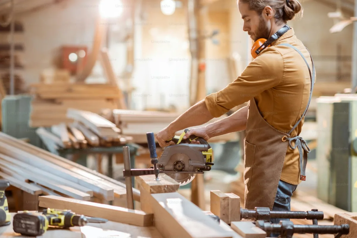 A carpenter cutting timber with a circular saw at a workbench