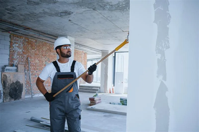 Hire painting estimating services: painter with roller on pole painting a wall inside a building under construction