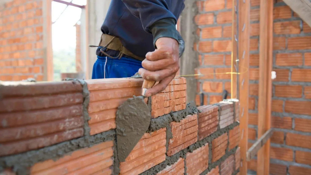 A bricklayer spreading mortar along a course of brickwork