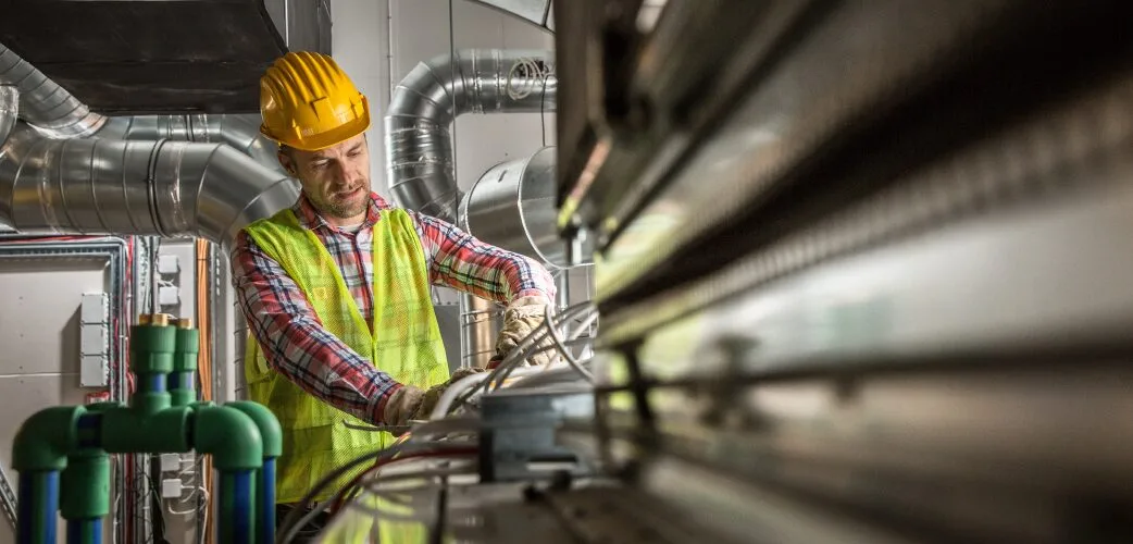 An engineer inspecting pipework and ducting in a plant room