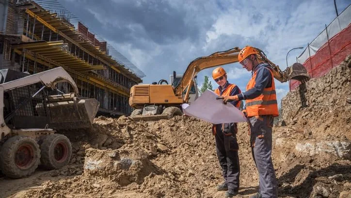 sitework estimating services: workers reviewing plans on an excavation site with heavy equipment