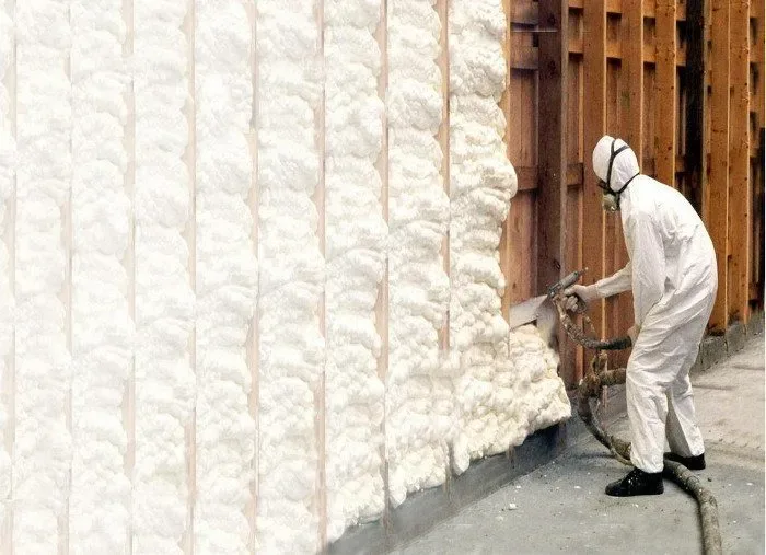 A worker spray-applying foam insulation to a timber-framed wall
